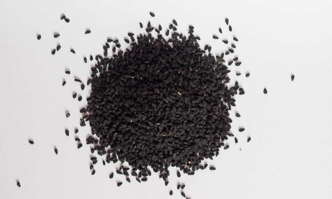 Graines de nigelle entières présentées en tas sur fond clair