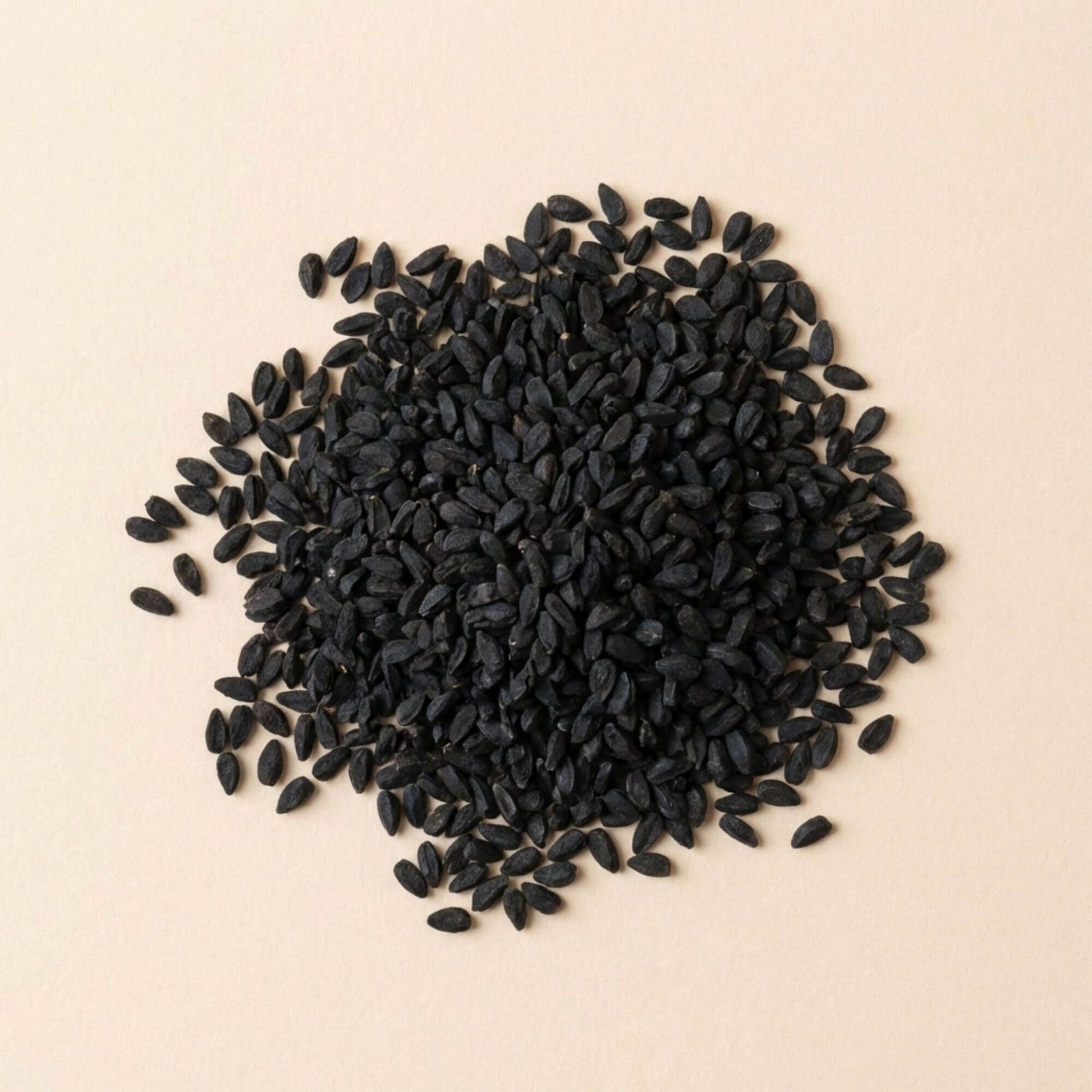 Graines de nigelle Habba Sawda entières en vrac, disposées sur fond beige clair, graines noires non broyées.