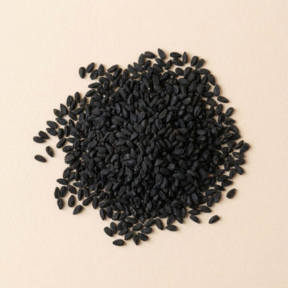 Graines de nigelle Habba Sawda entières en vrac, disposées sur fond beige clair, graines noires non broyées.