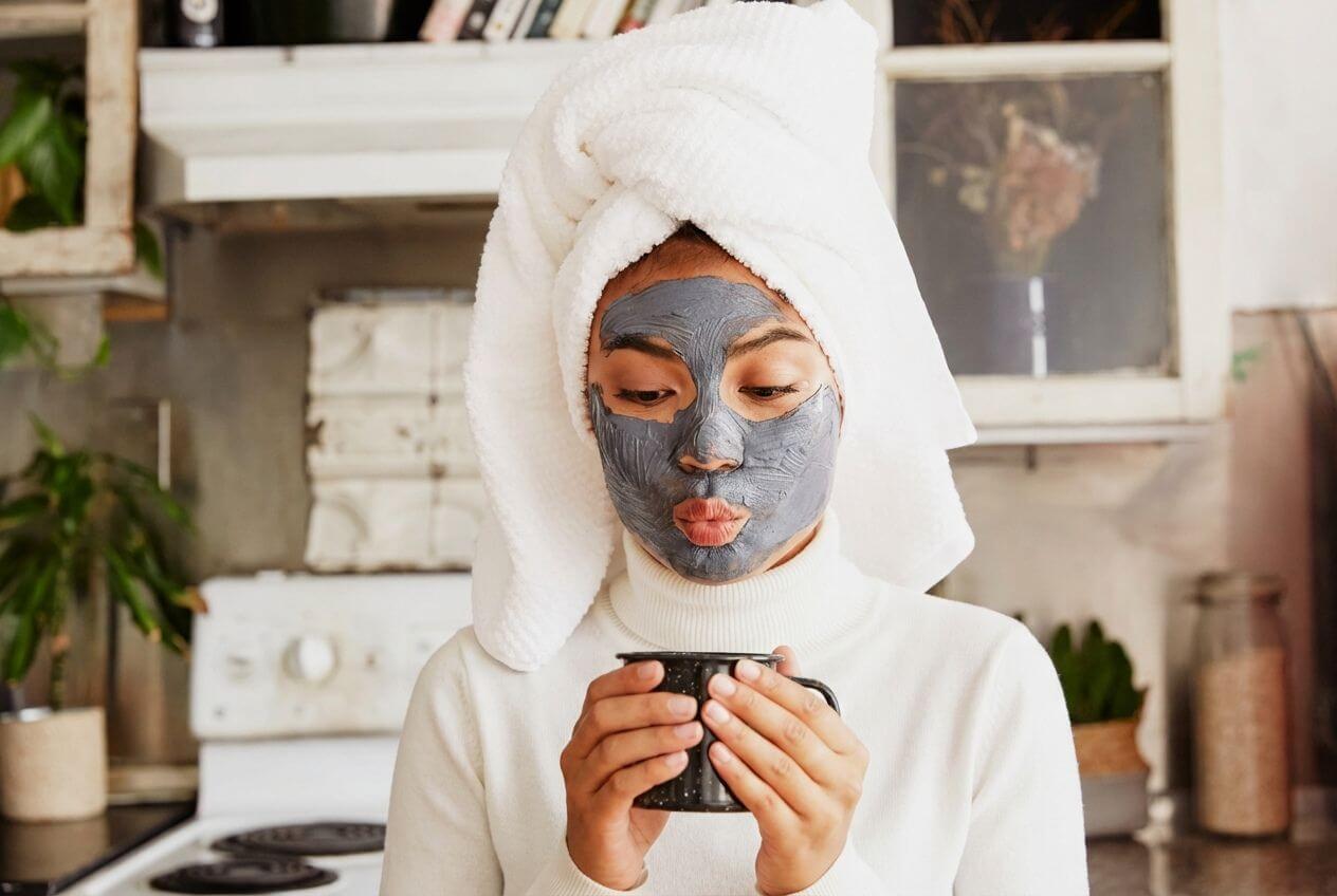 Personne appliquant un masque naturel sur le visage tout en tenant une tasse chaude, illustrant un moment bien-être et l’inscription à la newsletter Naturo Sunna.