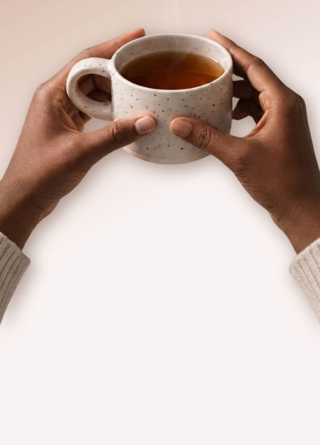 Main tenant une tasse en céramique beige mouchetée contenant une infusion chaude, avec une vapeur légère, dans une ambiance douce et lumineuse évoquant un moment de calme et de bien-être naturel.