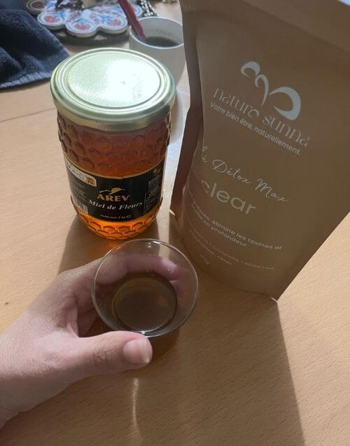 Photo client montrant la tisane Clear Détox Max de Naturo Sunna accompagnée de miel et d’une tasse d’infusion, illustrant une préparation naturelle à la maison.