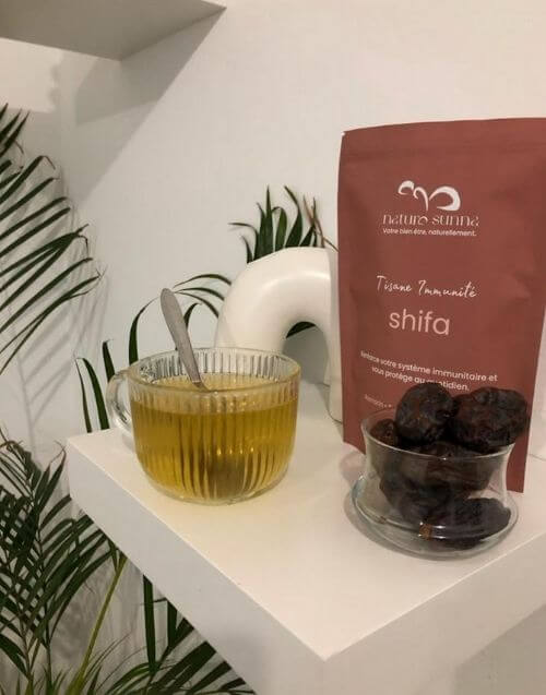 Photo client montrant la tisane Shifa Immunité Naturo Sunna avec une tasse d’infusion et des ingrédients, illustrant une préparation simple et réelle du produit à la maison