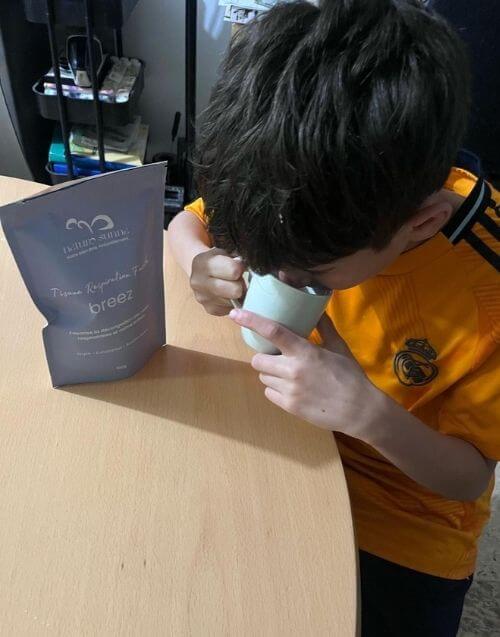 Photo client de la tisane Respiration Facile Breez Naturo Sunna, montrant un enfant en train de boire une tasse d’infusion, illustrant une utilisation réelle du produit à la maison dans un contexte quotidien.